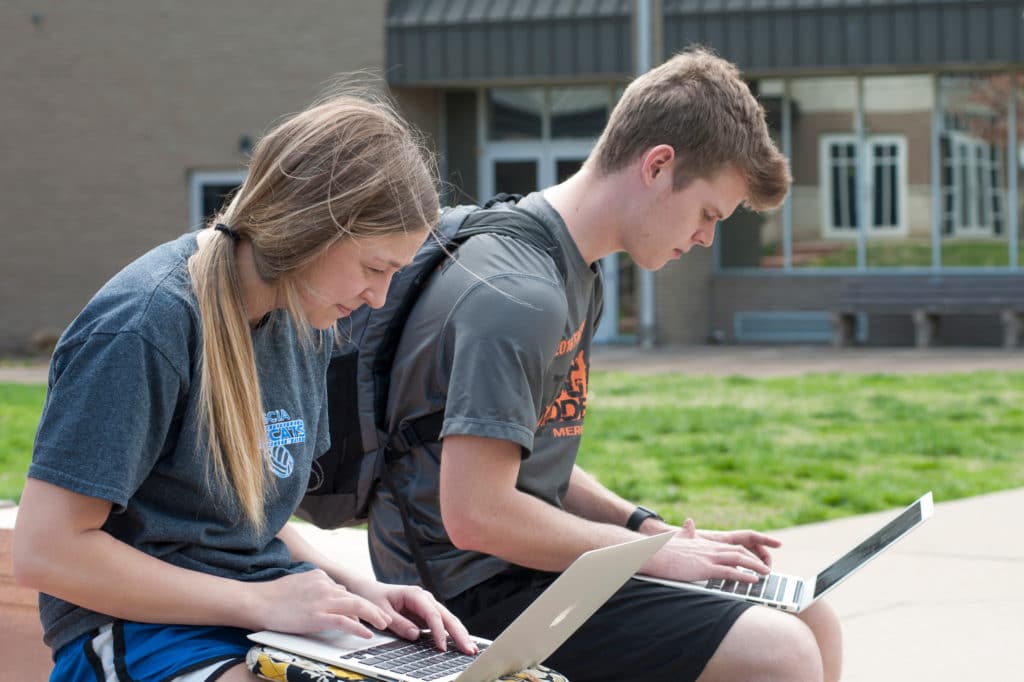 Two students doing work with computers in the quad