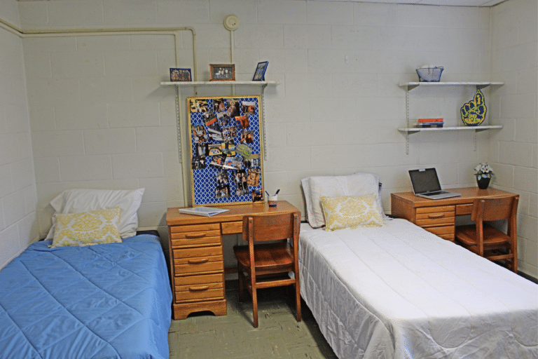 The inside of a double occupancy room inside of Merici Hall. There are two beds, two desks, and three shelves.