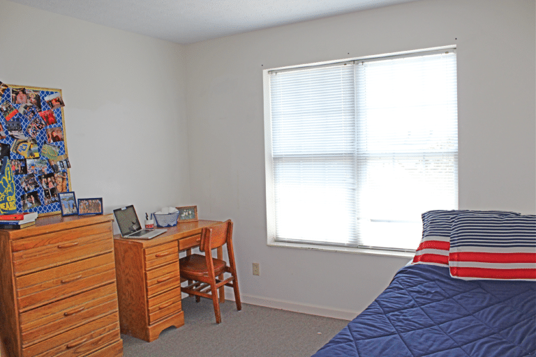 A bedroom inside of an apartment in Trustees Hall. The room includes a bed, desk, and dresser.