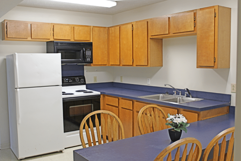 The kitchen inside of on apartment in Young Hall. There is a refrigerator, stove, microwave, sink, and table.
