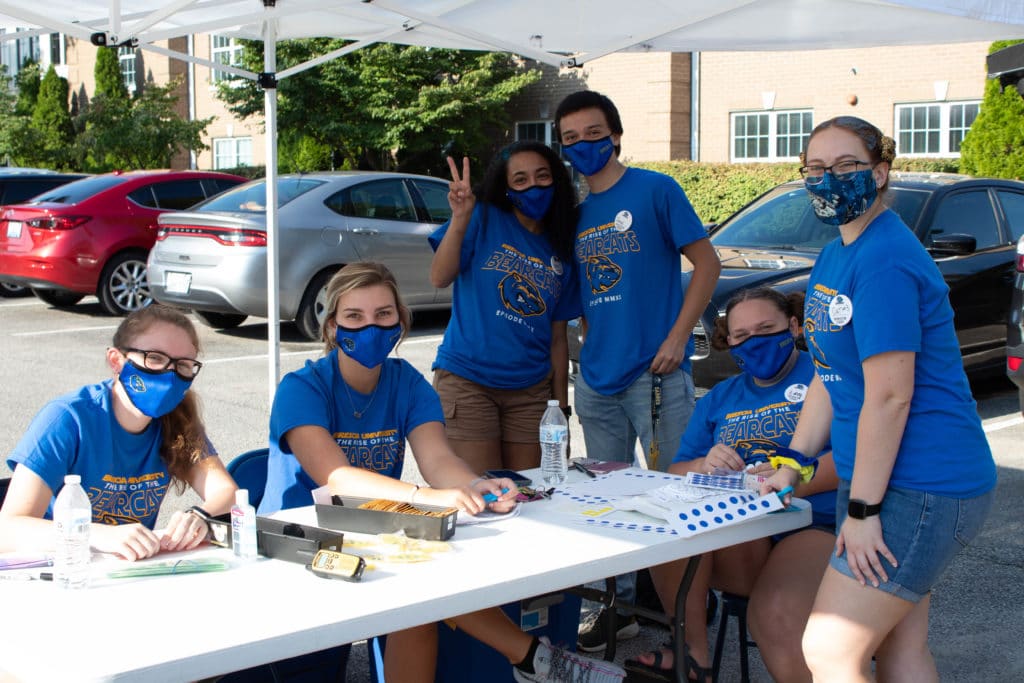 Group of students, wearing blue masks and matching blue shirts, are at a table outside for Orientation