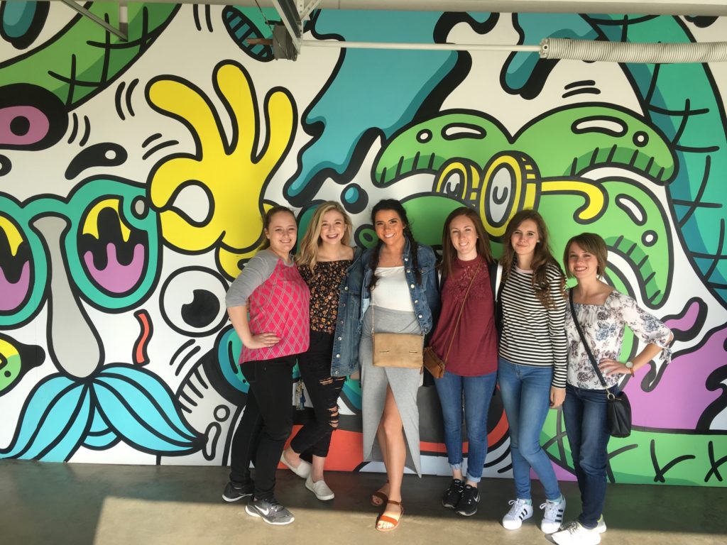 Students standing in front of a colorful mural.