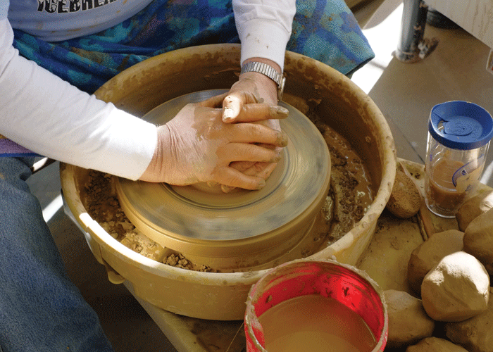 Hands forming clay on a pottery wheel